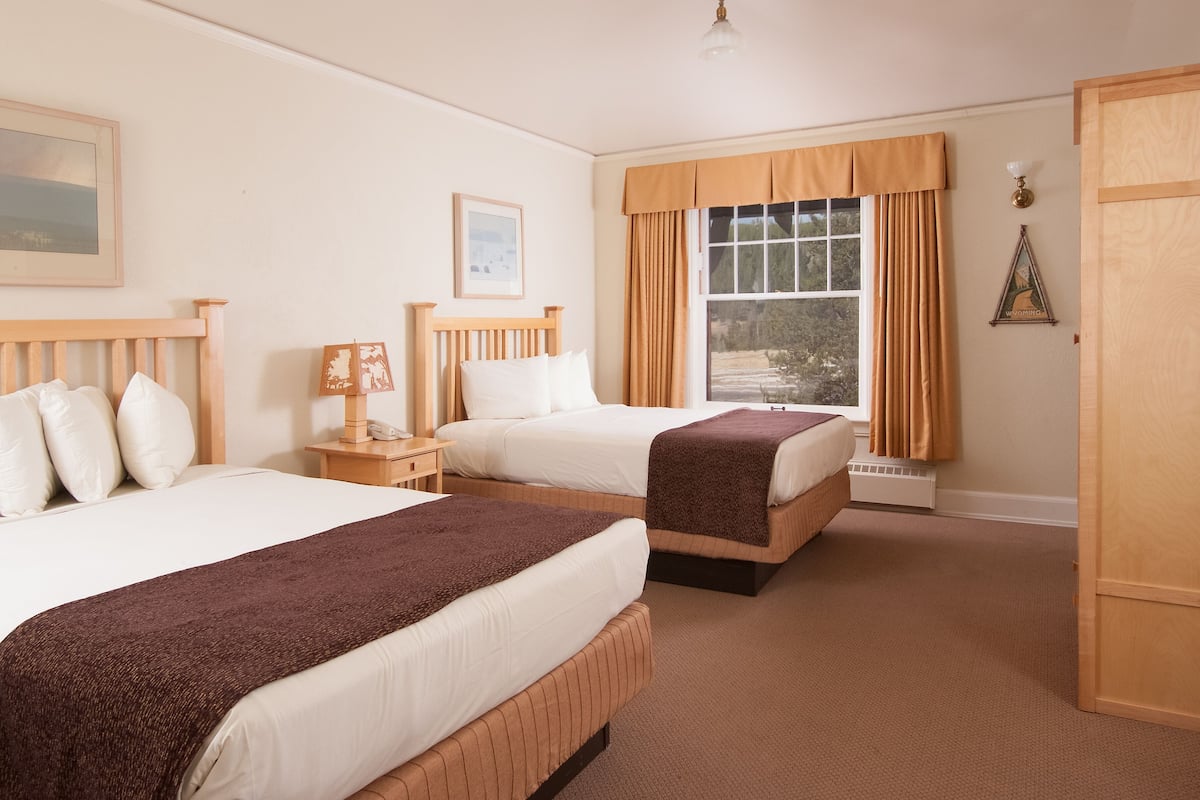 Une chambre d’hôtel avec deux lits, une table de chevet avec une lampe, un tableau encadré au mur et une fenêtre avec des rideaux.