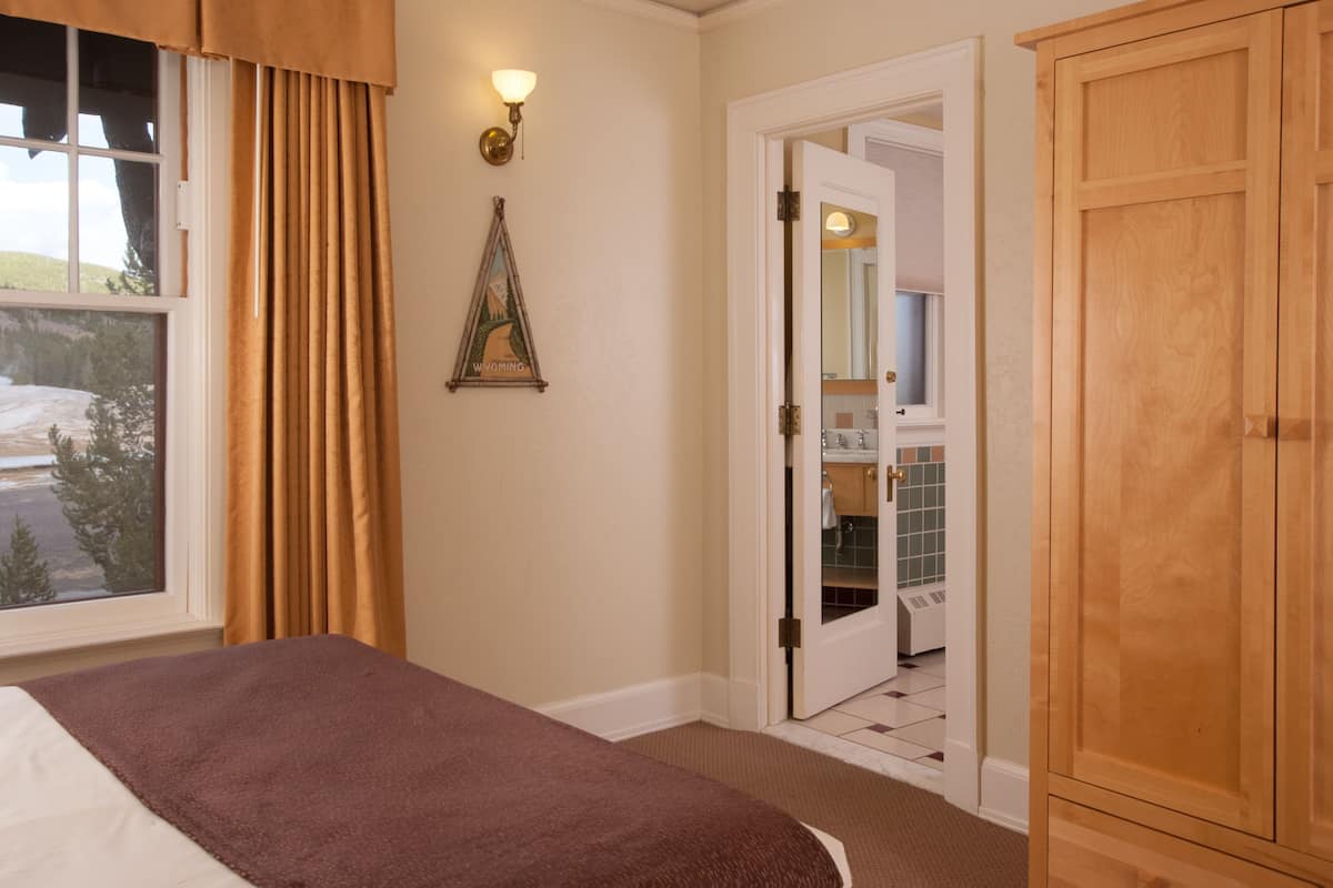 Une chambre d’hôtel avec un lit, une armoire en bois, une salle de bain visible à travers une porte ouverte et un tableau encadré au mur.