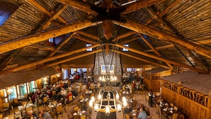 Un restaurant spacieux avec de hauts plafonds en bois et un lustre central. Les tables sont disposées autour d’un couloir central, et les murs sont ornés d’éléments en pierre.