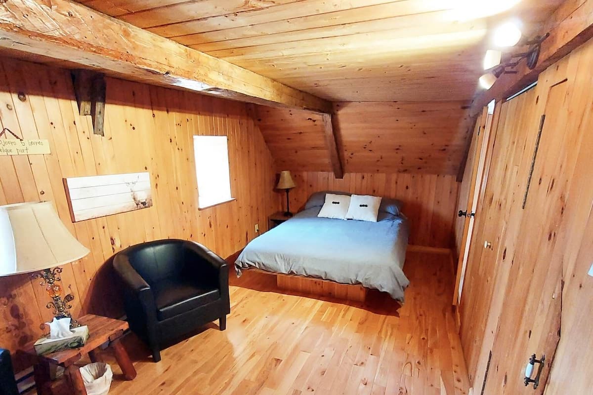 Camera da letto in una baita di legno, con un letto, una sedia, un tavolino e una finestra.