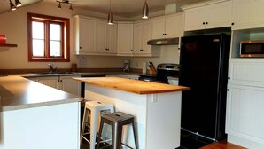 Una cocina con armarios blancos, un refrigerador negro, una encimera de madera y una ventana.