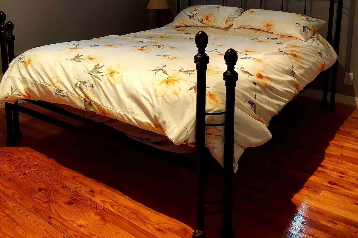 Una camera da letto con un letto, pavimento in legno, una finestra con tende e una lampada.
