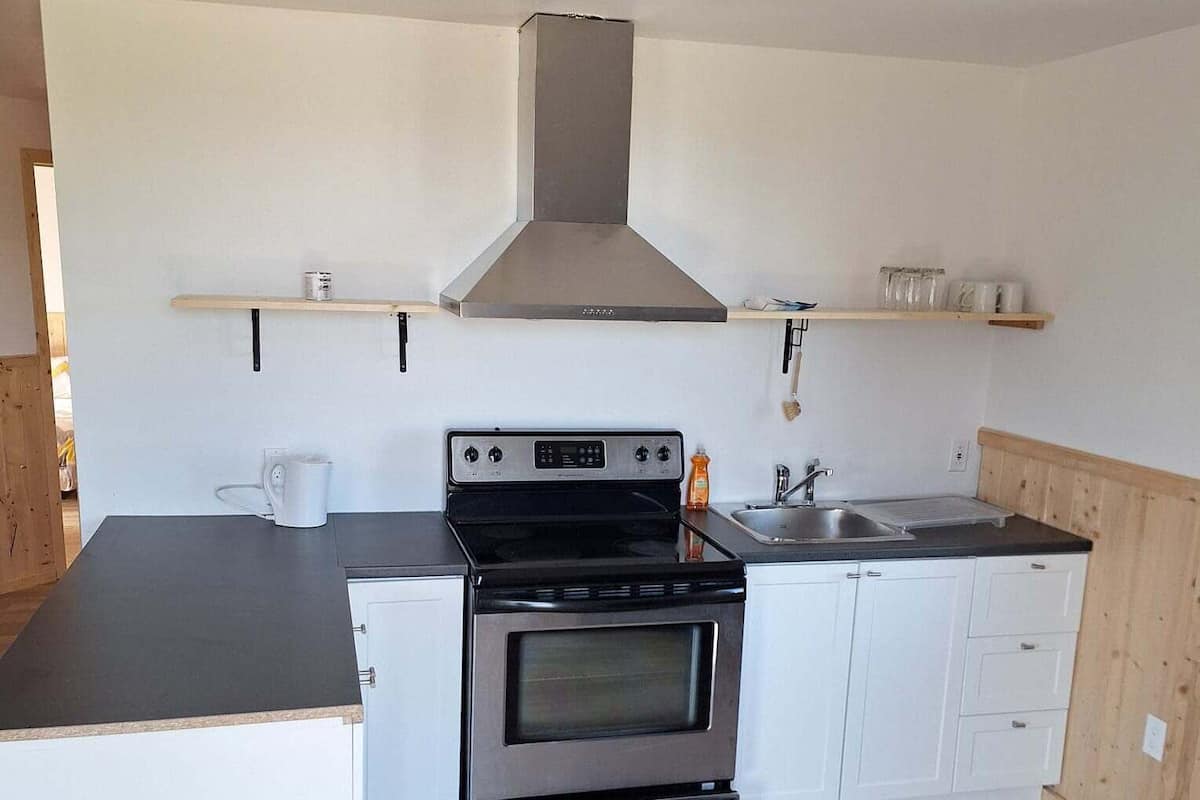 Una cucina compatta con forno integrato, lavello e mensole in legno sopra.