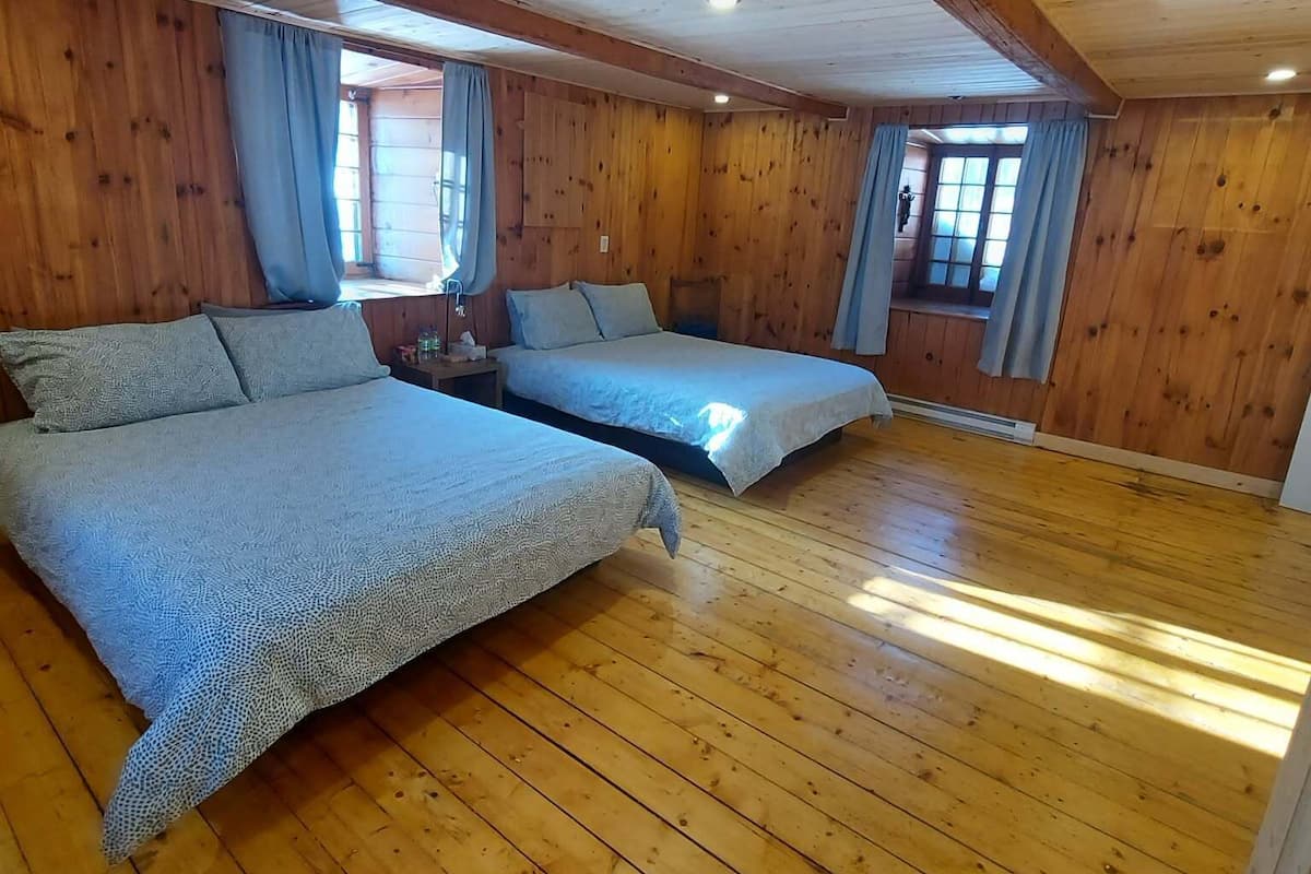Una stanza con rivestimento in legno, due letti, una finestra con tende e soffitto in legno.