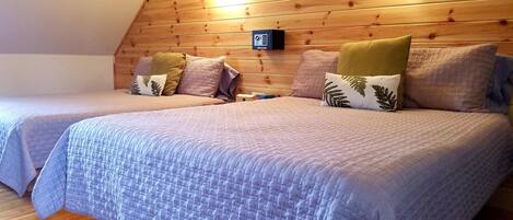 A cozy bedroom with two beds, wooden paneling on the ceiling, and a mounted thermostat.