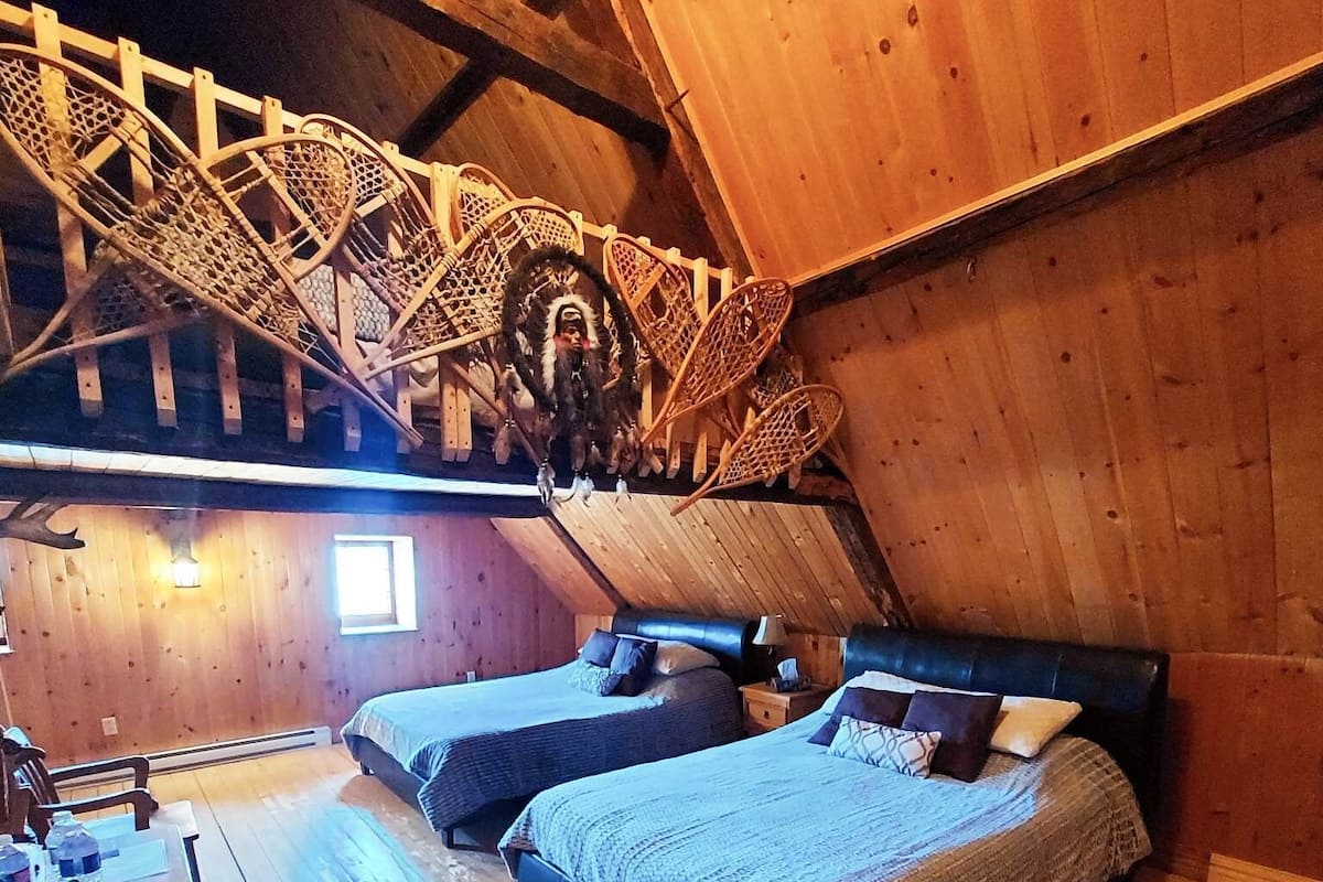 Una camera da letto mansardata accogliente, con due letti, travi in legno, una scala rustica e un piccolo oblò.