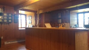 Interior de madera con una mesa de recepción, cuadros en las paredes y una cruz en el techo.