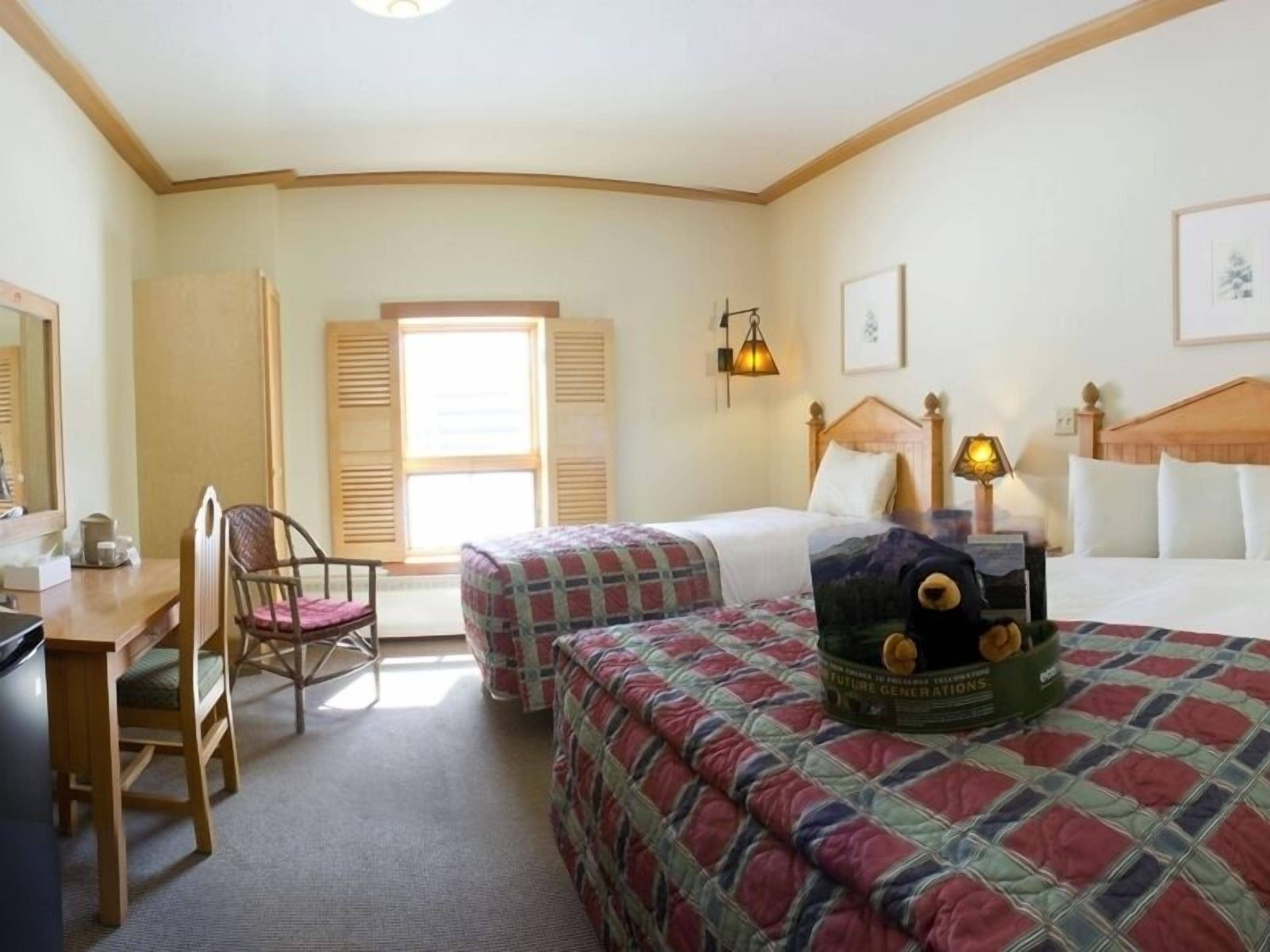 Habitación de hotel con dos camas, un escritorio, una silla y una ventana con contraventanas.