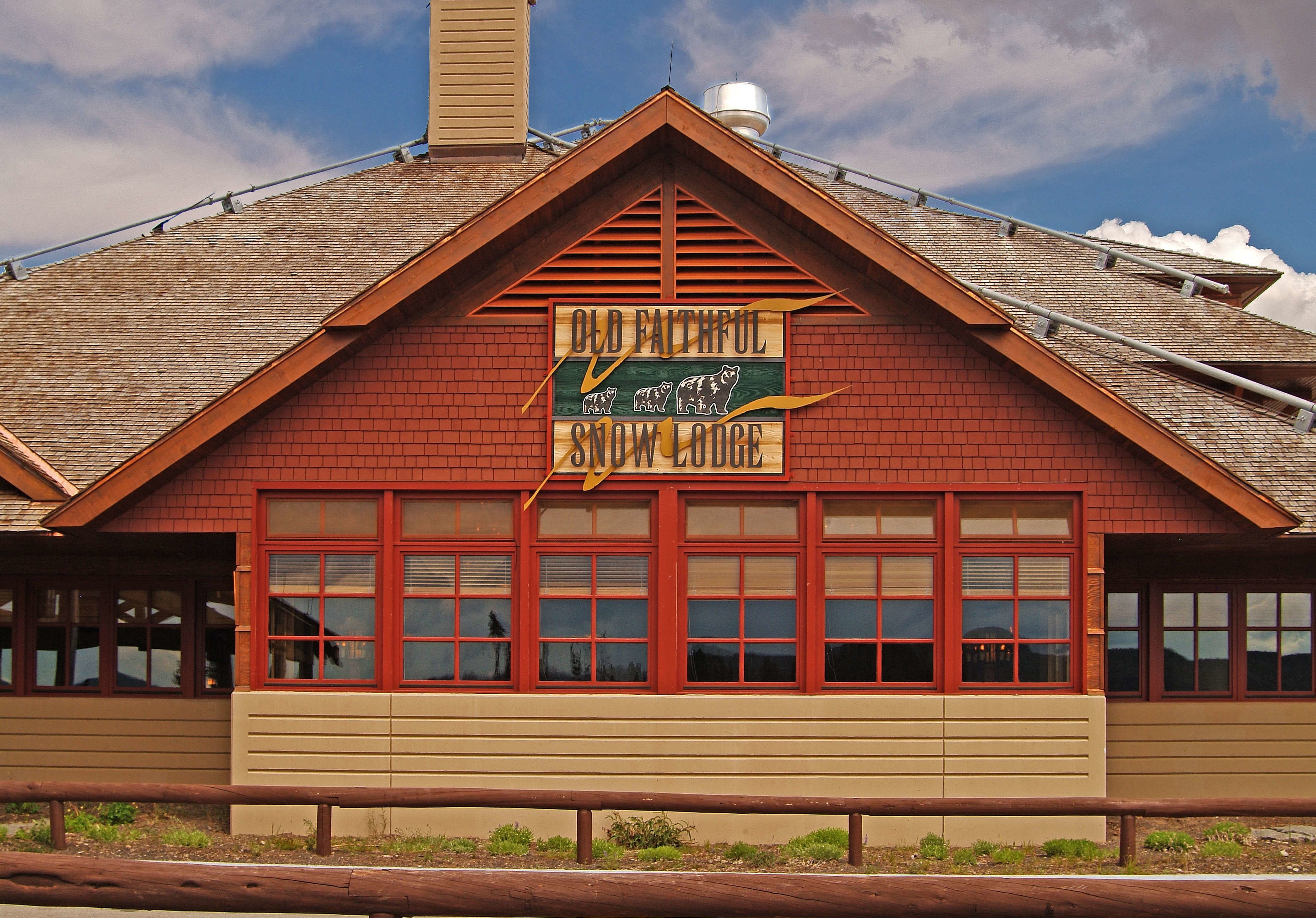 A building with a red brick facade, a green sign reading "Old Faithful Snow Lodge," and a wooden roof.