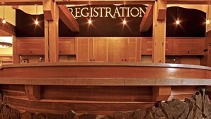 A wooden registration desk with a stone base, surrounded by wooden beams and a stone wall. - Old Faithful Snow Lodge & Cabins - Inside the Park (Yellowstone National Park)
