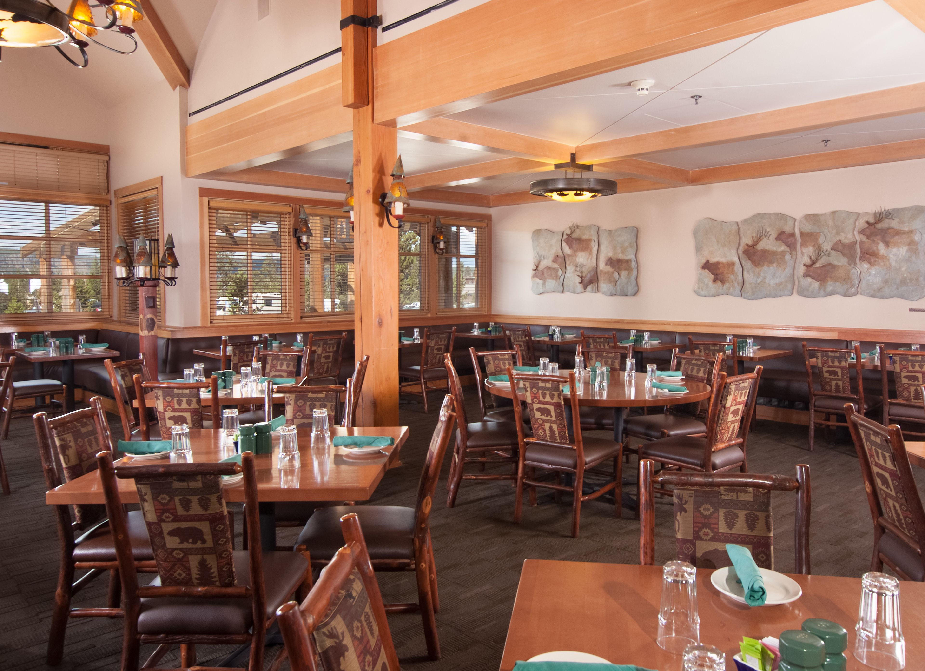 A restaurant with wooden tables and chairs, large windows, and a high ceiling.