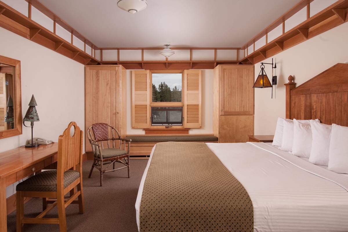 A hotel room with a large bed, wooden headboard, a desk with a chair, a window with shutters, and a television.