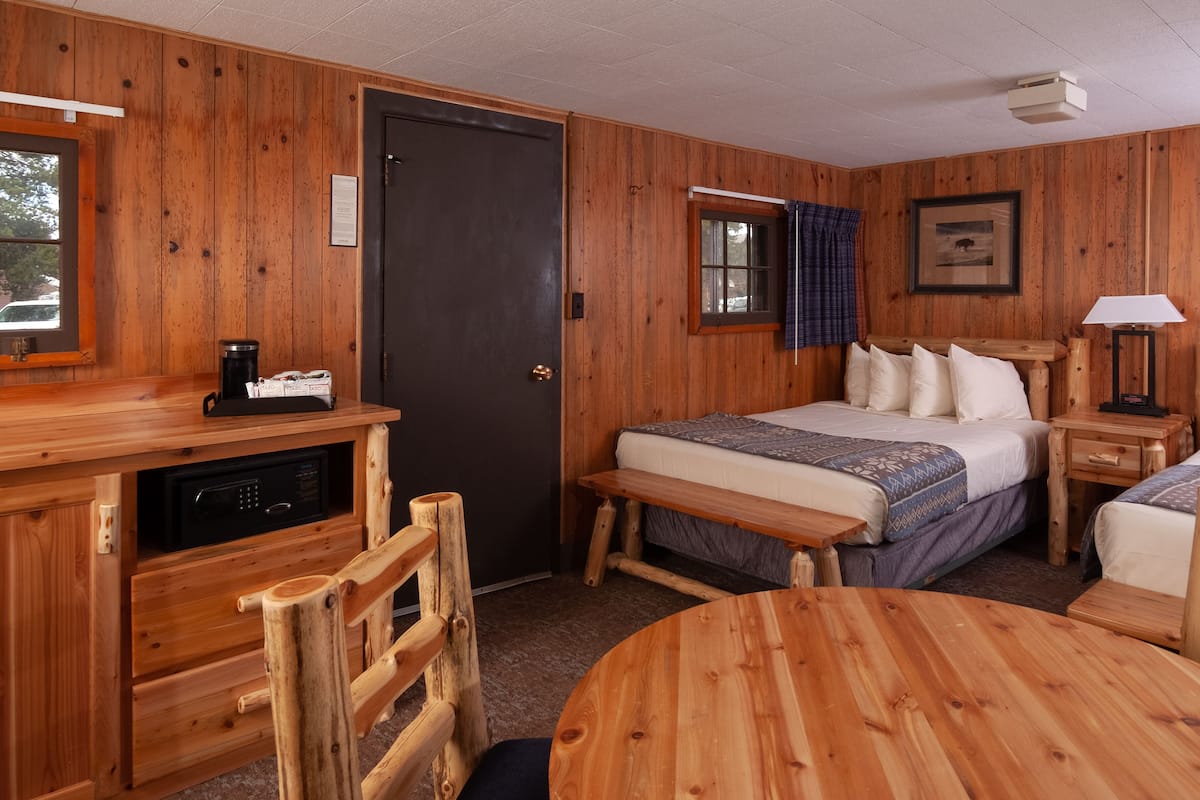 A wooden cabin room with a bed, bedside table, lamp, and a small desk with a coffee maker.