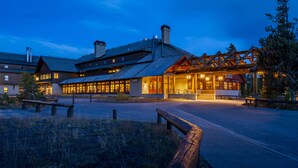 A lodge with a covered entrance, a parking area, and a building with multiple windows. - Old Faithful Snow Lodge & Cabins - Inside the Park (Yellowstone National Park)