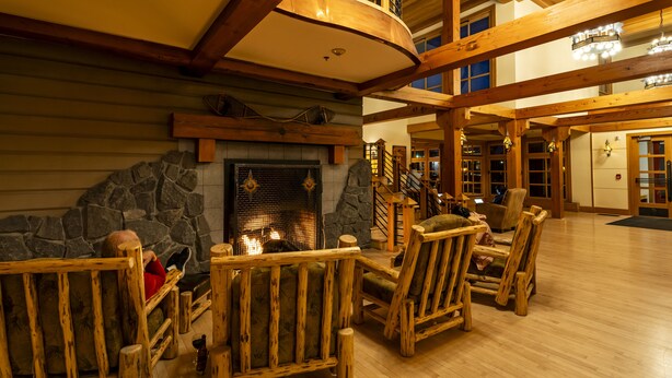 A spacious lodge interior with a stone fireplace, wooden furniture, and a high ceiling with exposed beams. - Old Faithful Snow Lodge & Cabins - Inside the Park (Yellowstone National Park)