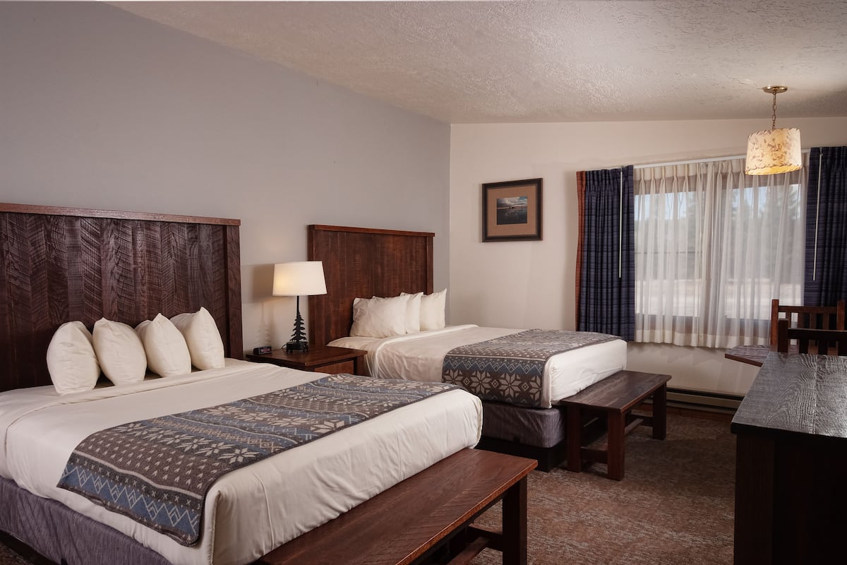 A hotel room with two beds, a desk, a chair, a lamp, and a window with curtains.