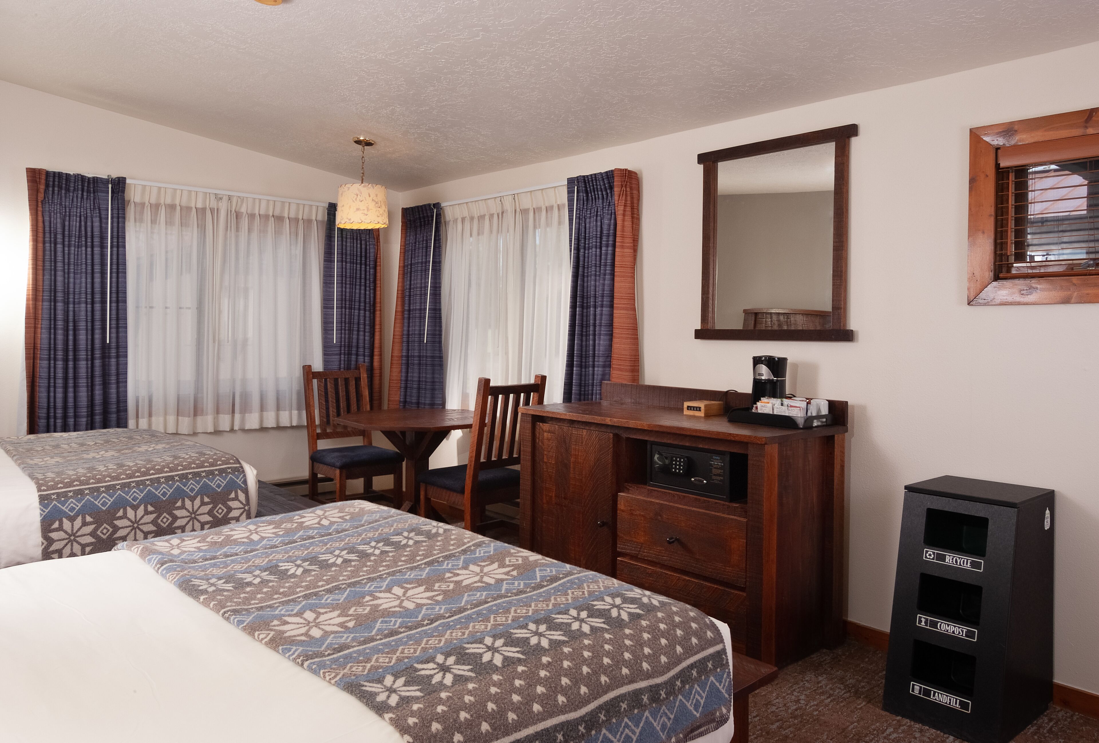 A hotel room with two beds, a wooden desk, a mirror, and a trash bin.