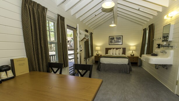 Une pièce avec une table en bois, un lit avec des oreillers, une table de chevet avec une lampe et un lavabo.