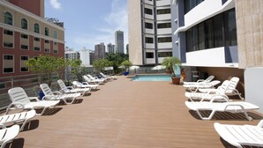 Un área de piscina en la azotea con tumbonas, piscina y vista panorámica de la ciudad.