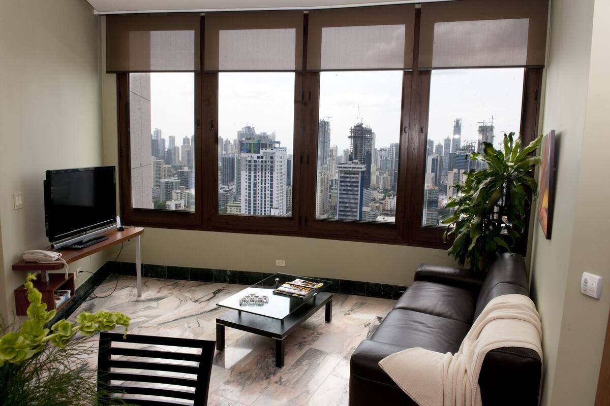 Ein Wohnzimmer mit großem Fenster, einem Flachbildfernseher, einem Couchtisch, einer Couch und einer Topfpflanze.
