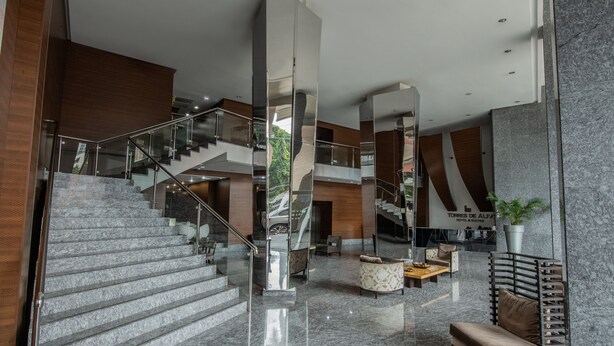 Un moderno vestíbulo de hotel con una escalera de mármol, zonas de estar y un espejo grande que refleja el espacio.