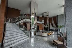 Un moderno vestíbulo de hotel con una escalera de mármol, zonas de estar y un espejo grande que refleja el espacio.