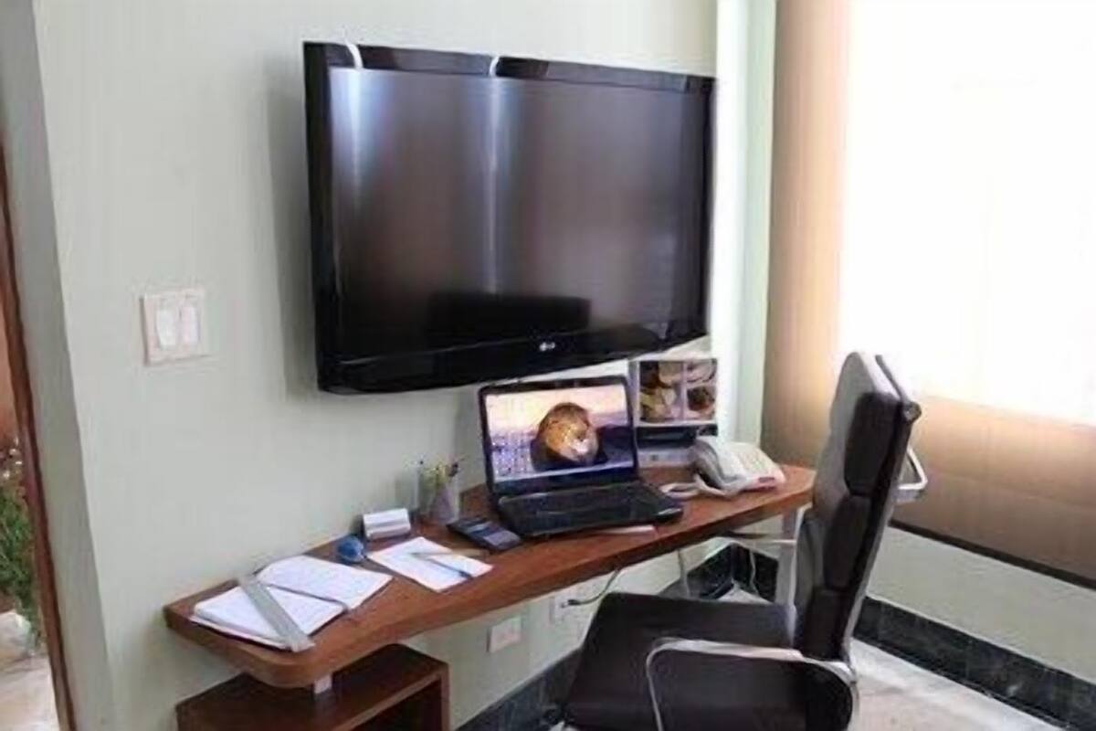 Ein Hotelzimmer mit Schreibtisch, Laptop, Telefon und an der Wand montiertem Fernseher.