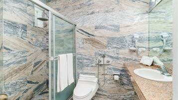 A bathroom with a glass shower enclosure, a toilet, a sink, and a marble-tiled wall.