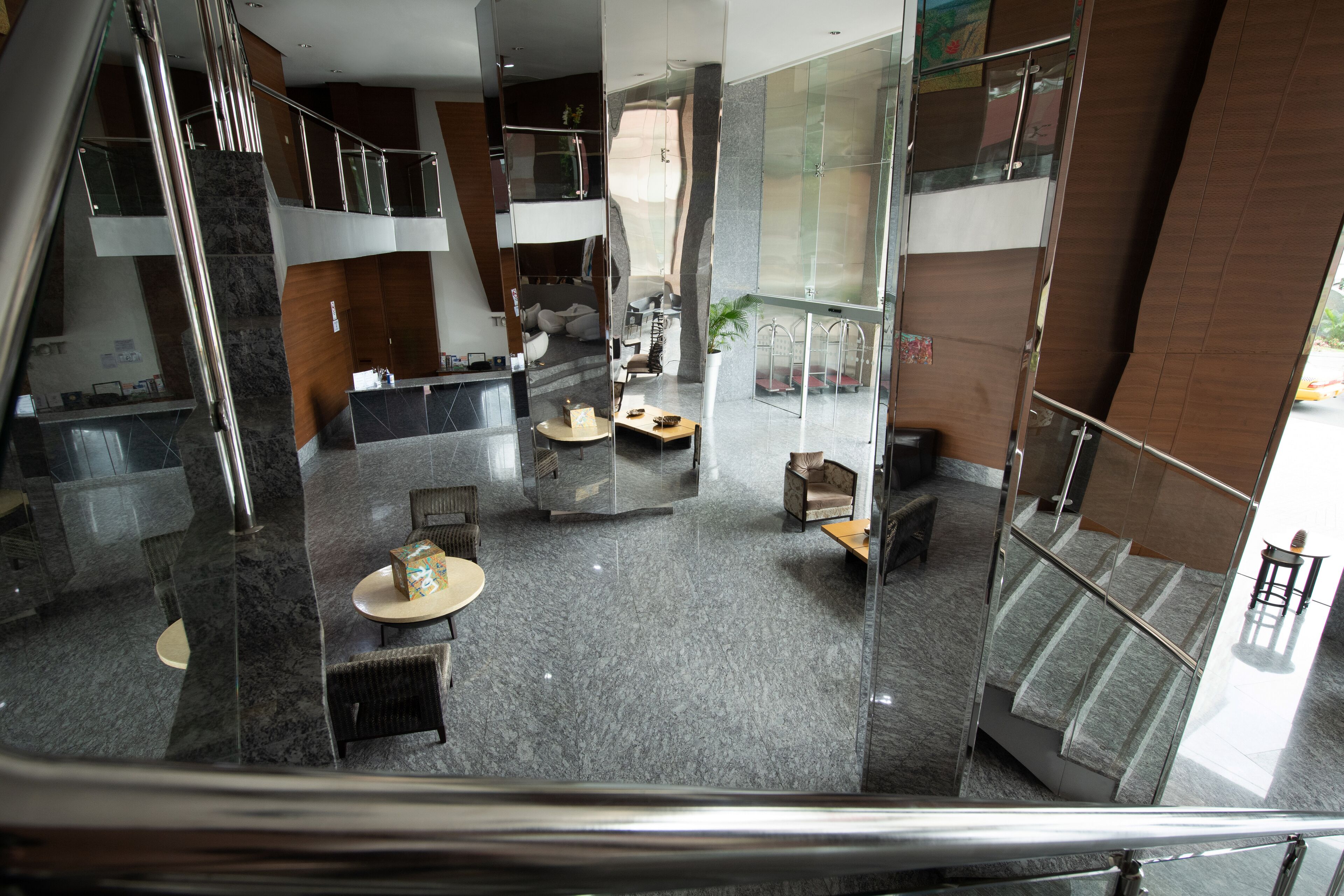Eine moderne Hotellobby mit Glaswand, einer Rezeption, Sitzbereichen und einer Treppe.