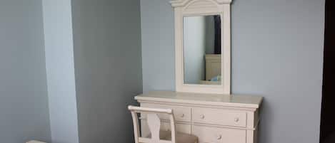 A bedroom with a bed, a dresser with drawers, a chair, and a mirror.