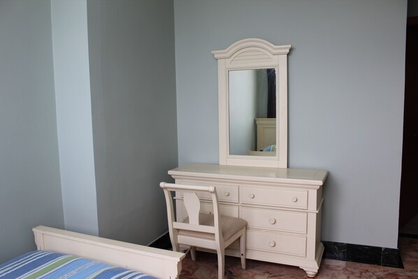 Un dormitorio con cama, cómoda con cajones, silla y espejo.