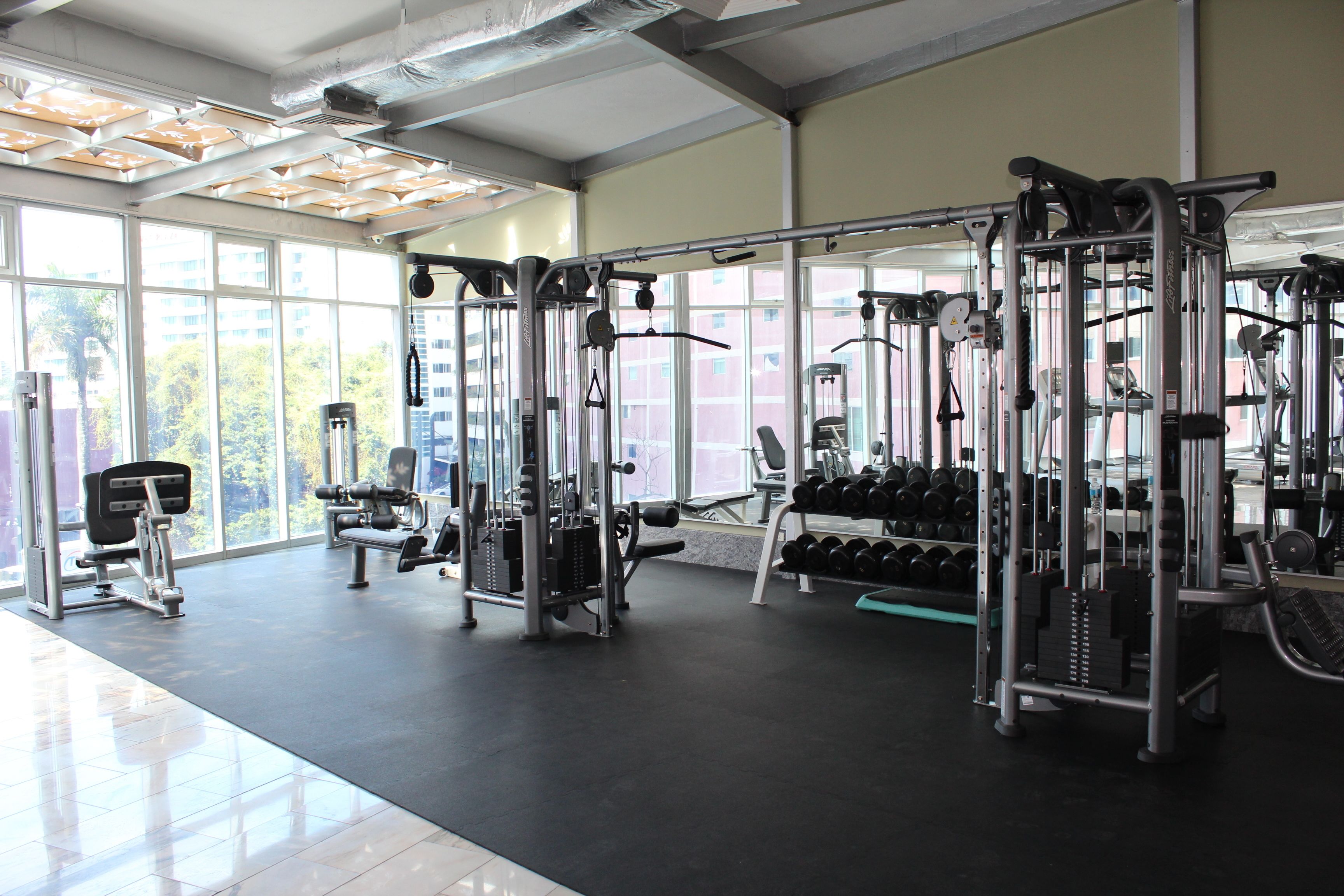 Une salle de sport équipée de divers appareils d’exercice, dotée de grandes fenêtres et présentant un design moderne et épuré.