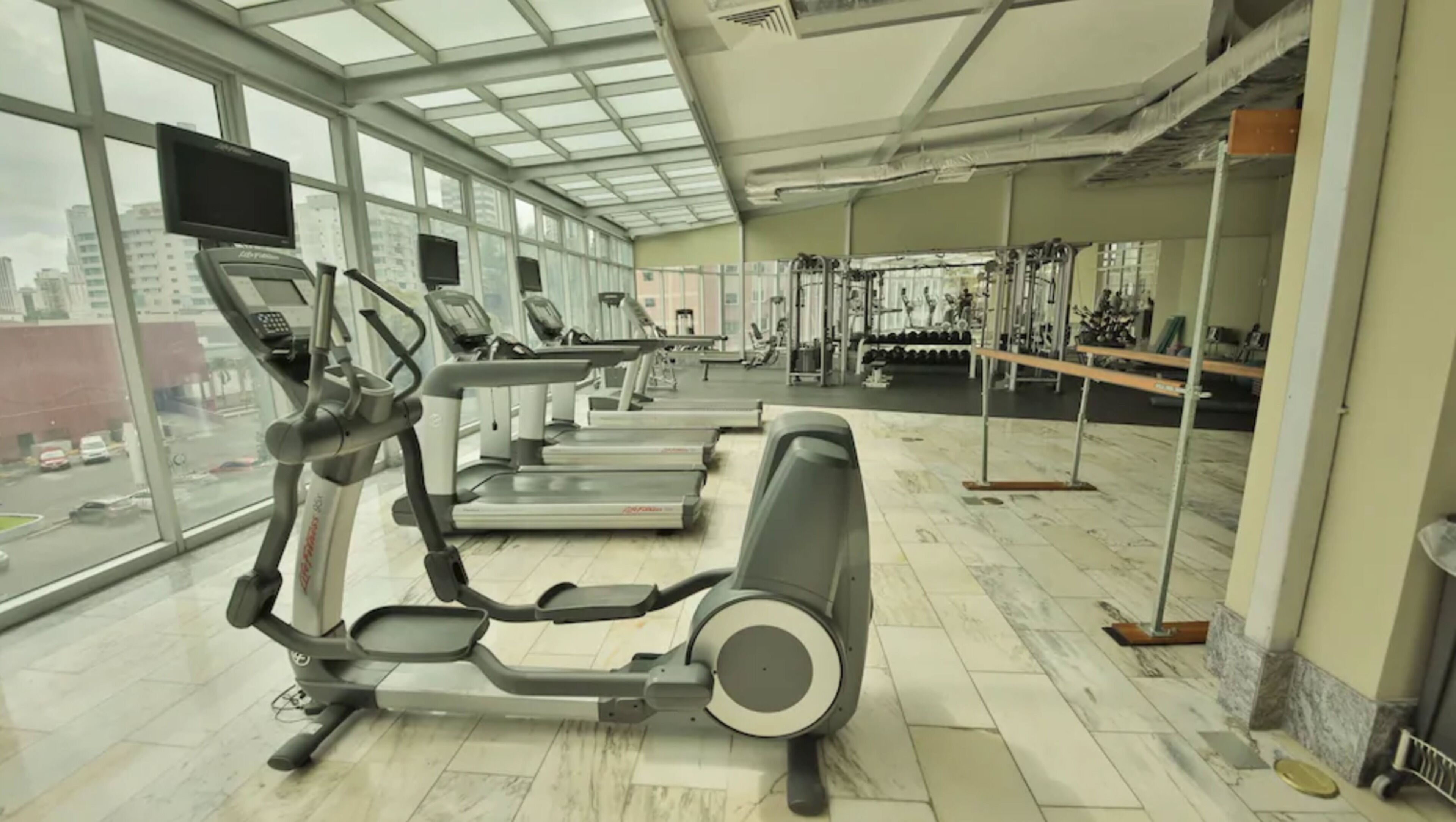 Un gimnasio con cintas de correr, máquinas de pesas y un amplio ventanal con vistas a la ciudad.