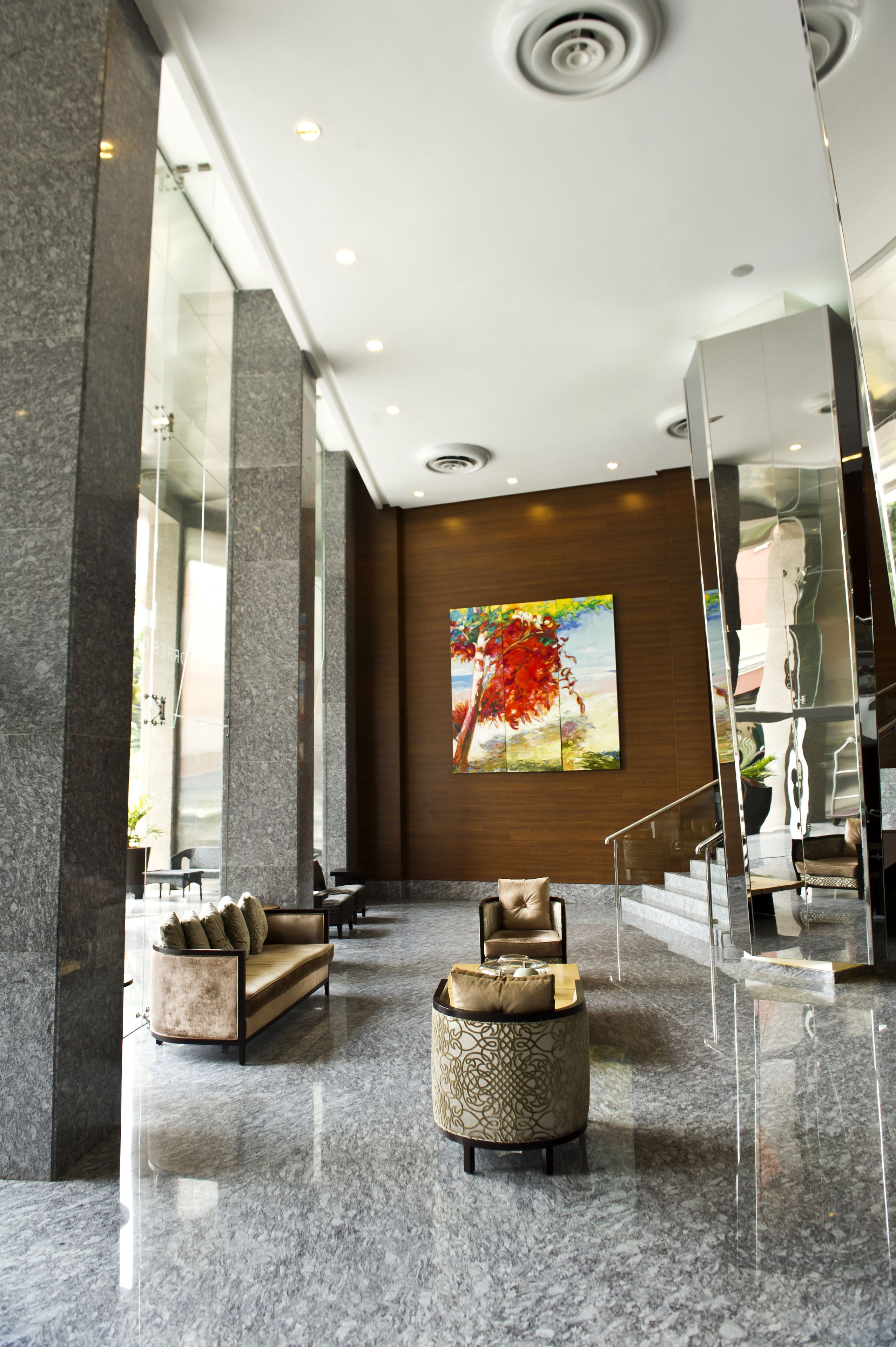 A lobby with marble flooring, a sofa, a round ottoman, and a staircase.