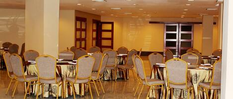 Un salón de conferencias con mesas y sillas redondas, equipado con proyectores y pantallas.