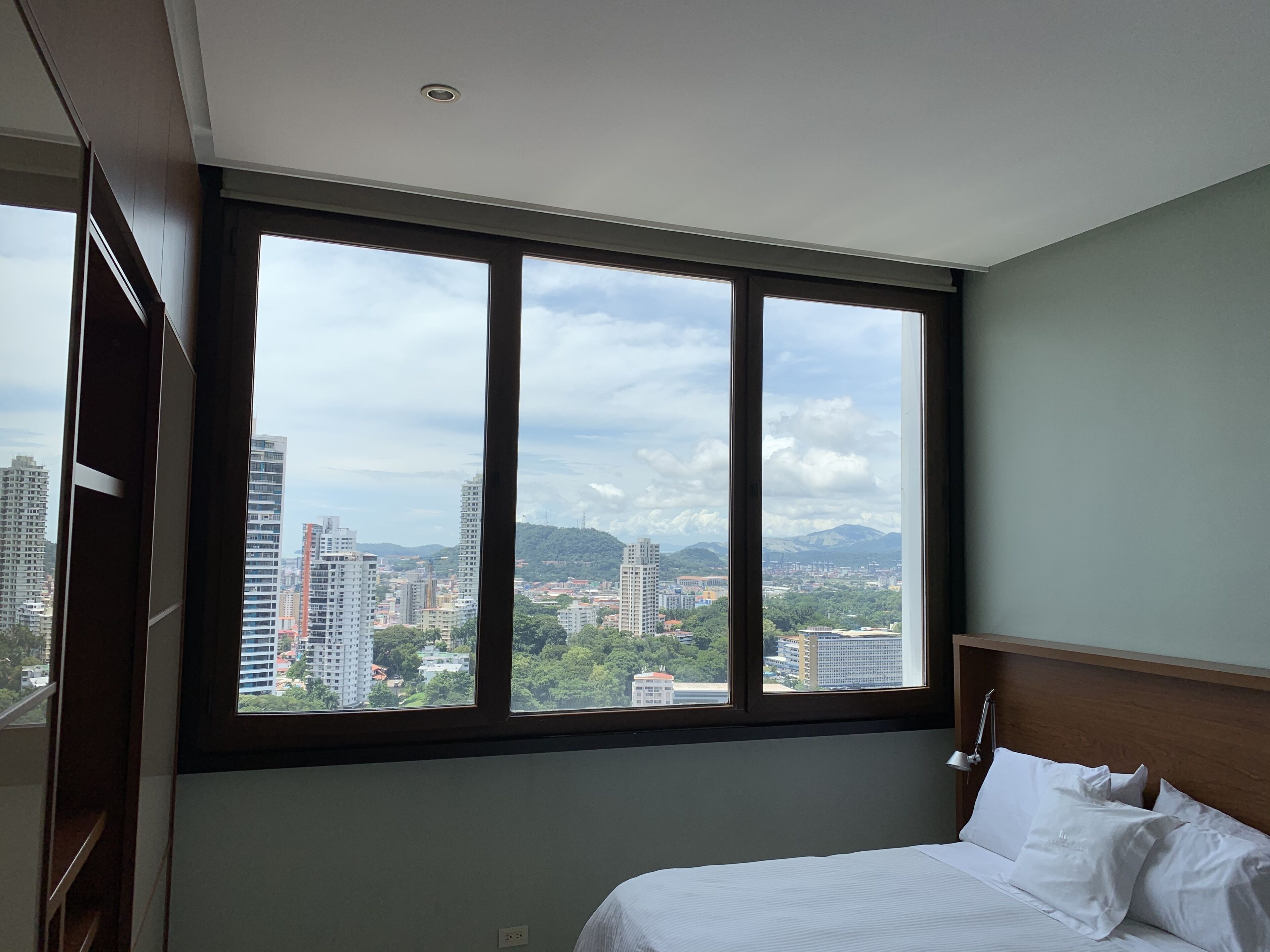 Una habitación de hotel con un ventanal grande, una cama y una mesita de noche.