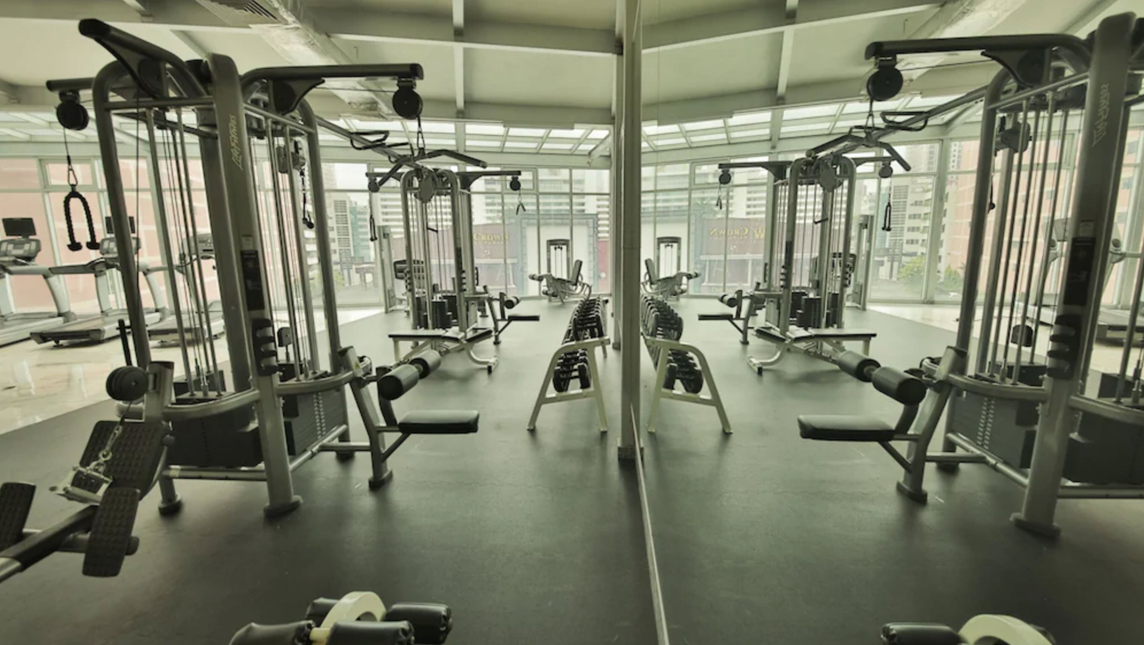 Un gimnasio con diferentes máquinas de ejercicio, paredes con espejos y ventanas amplias.