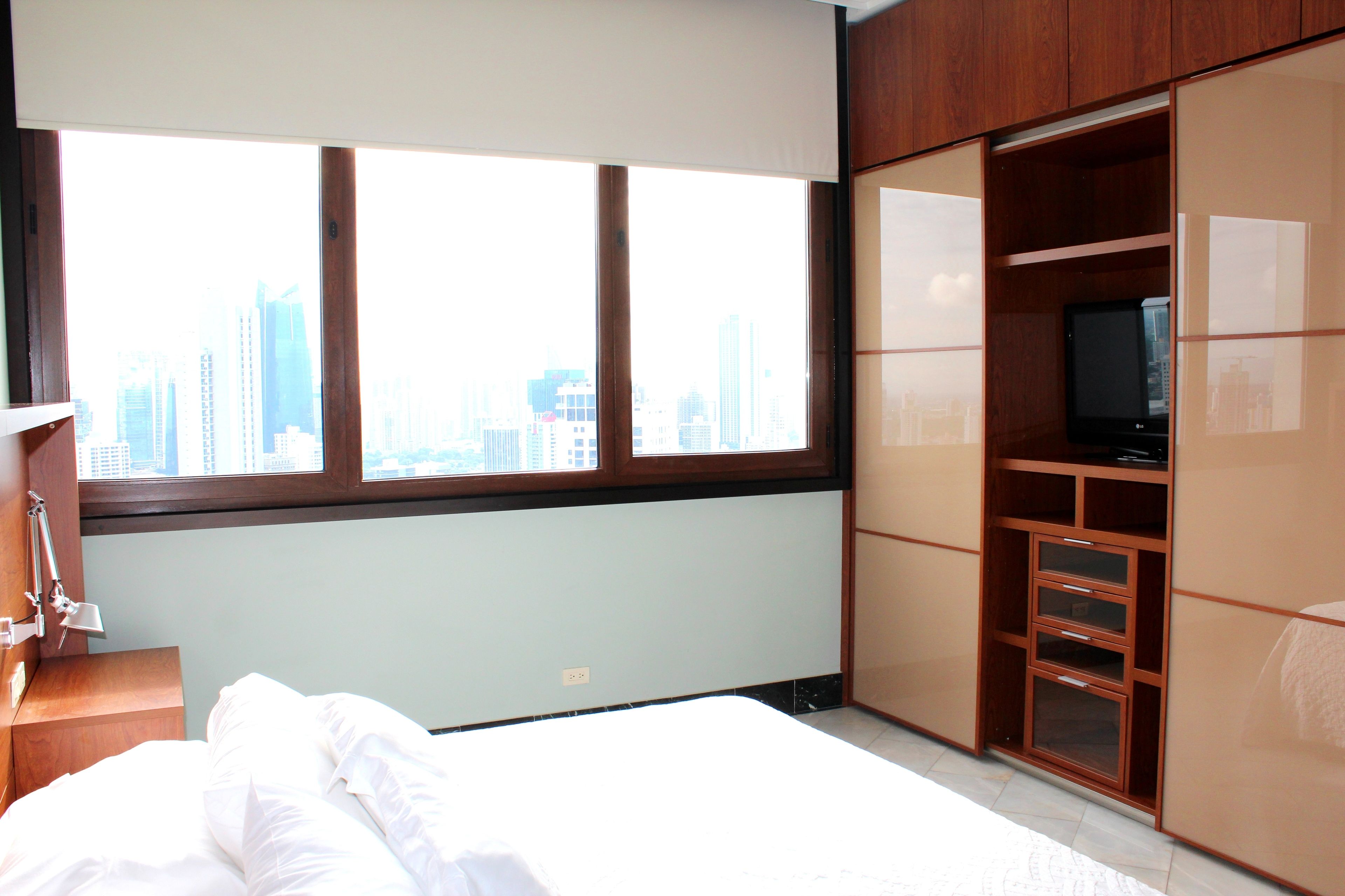 Una habitación de hotel con una cama, un televisor y un amplio ventanal con vista a la ciudad.