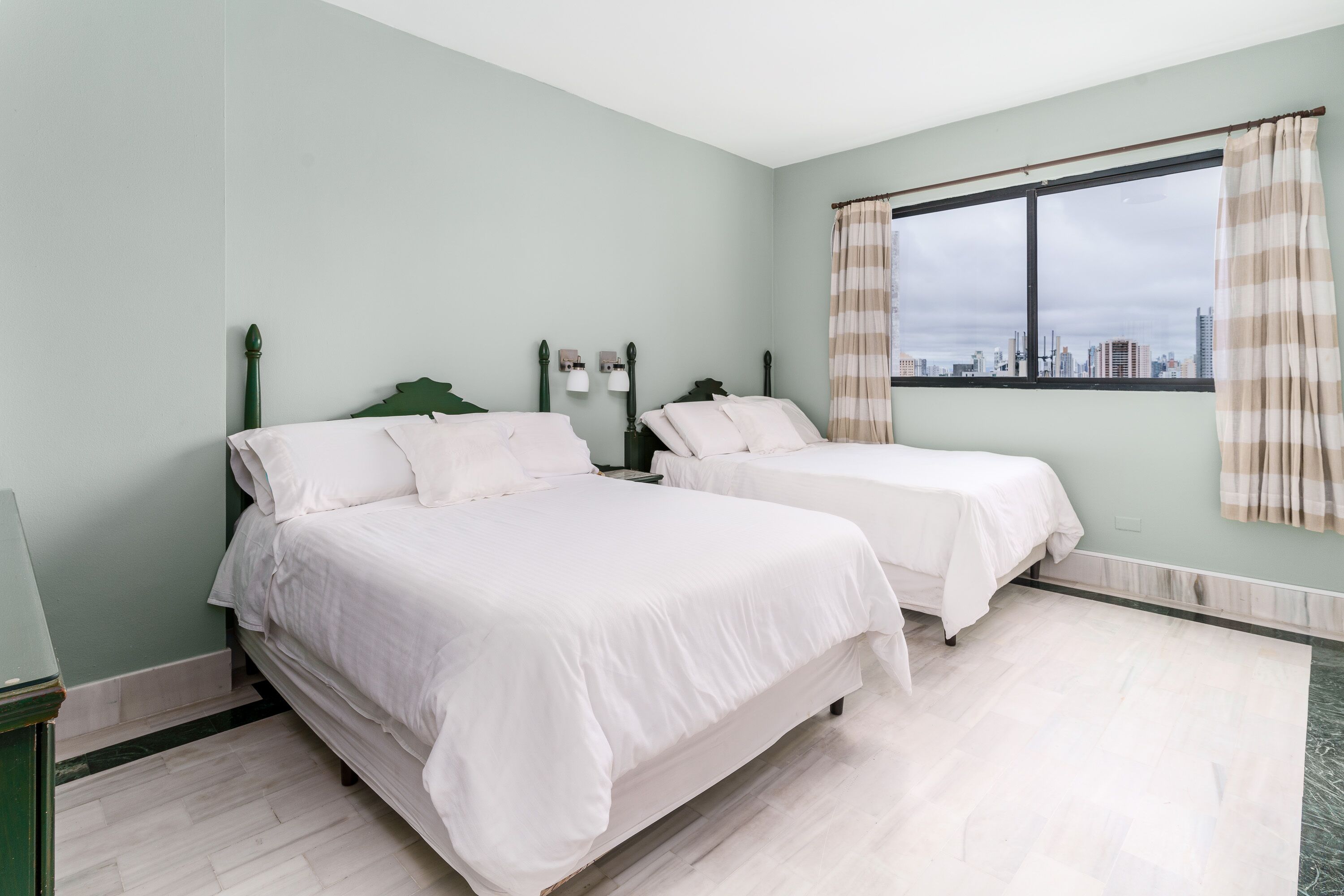 Una habitación con dos camas, una ventana con cortinas y vistas a la ciudad.