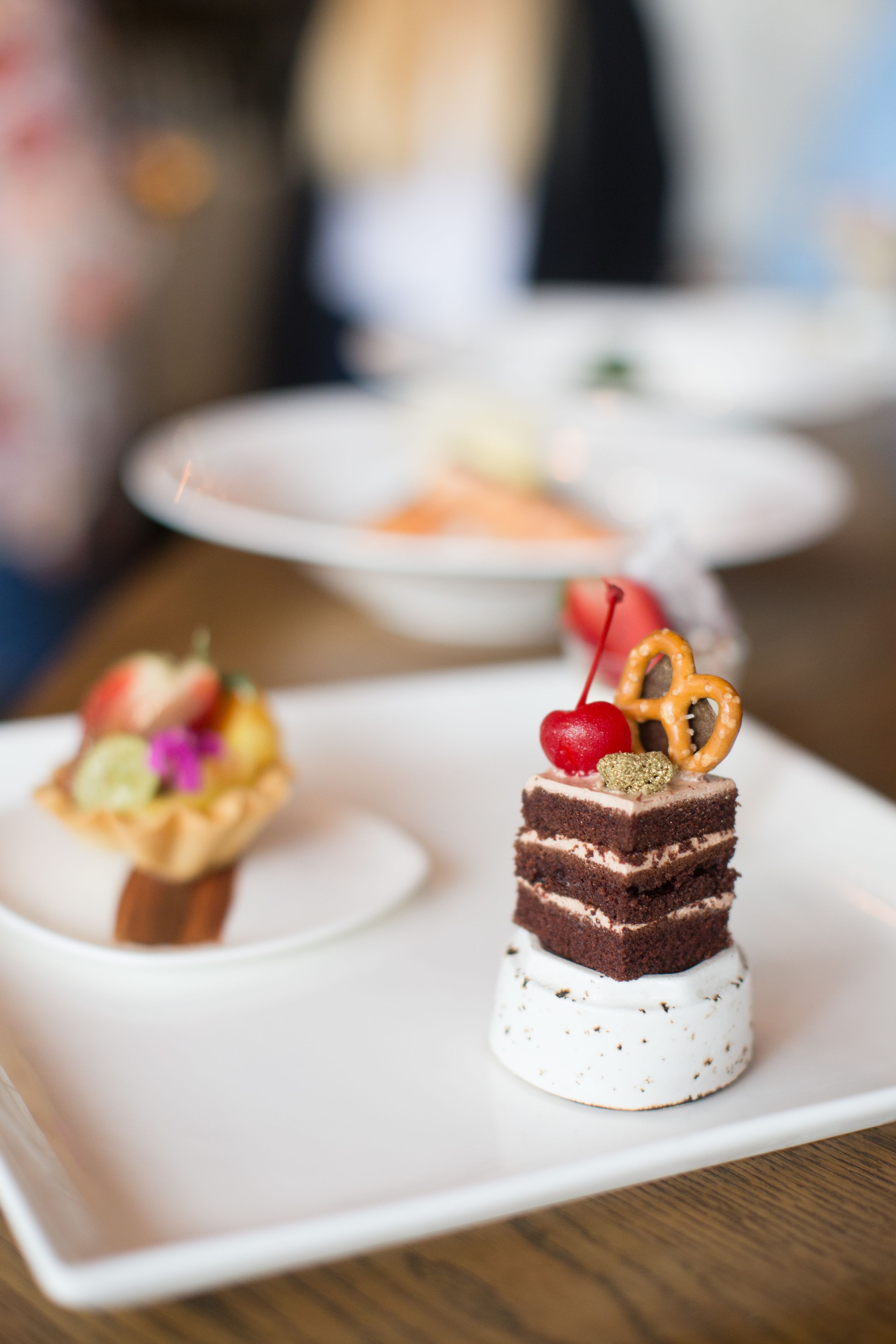 A dessert plate with a chocolate cake, a cherry, and a pretzel on a white plate.