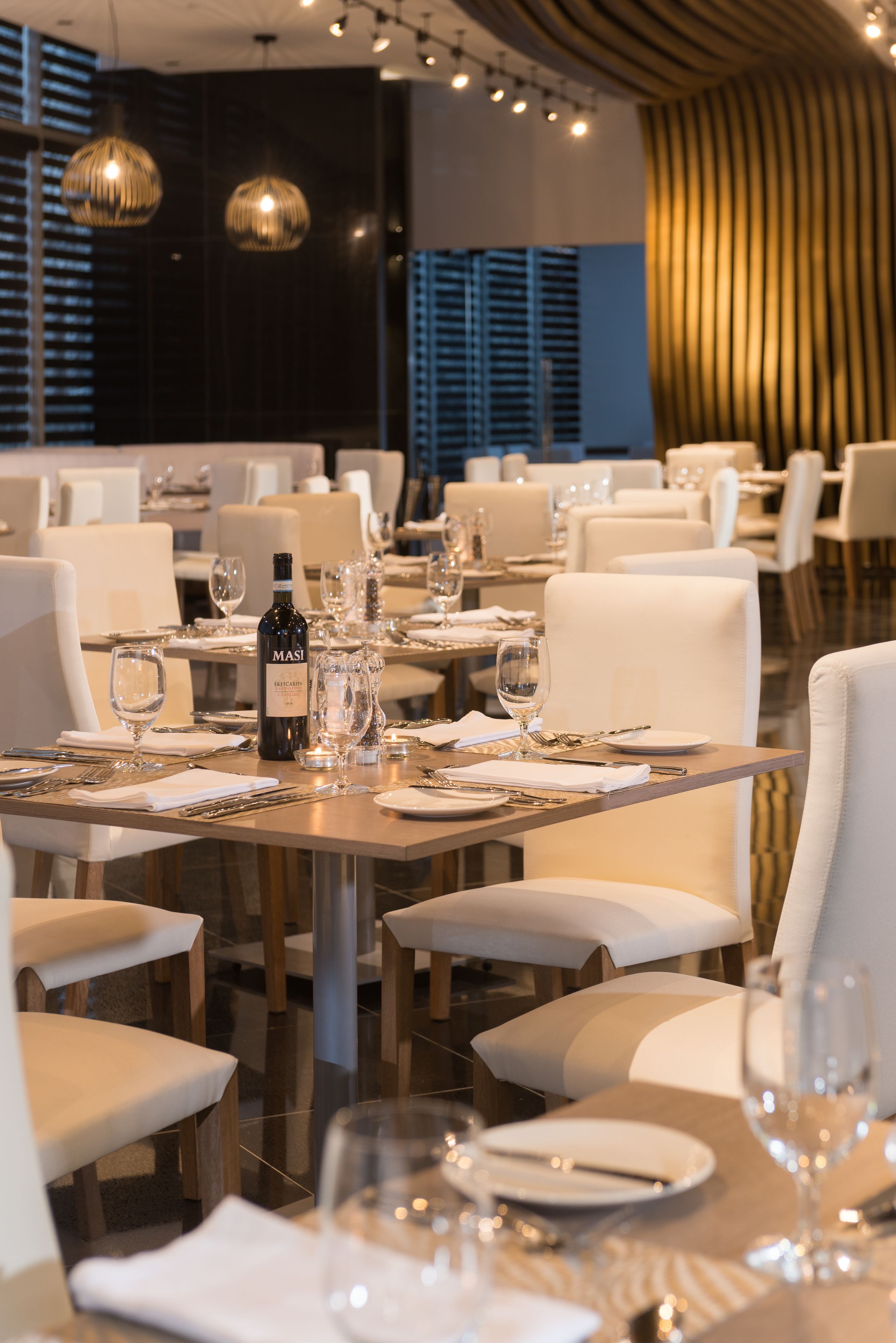 A restaurant with tables set for dining, featuring a bottle of Masi wine, glasses, and neatly arranged cutlery.