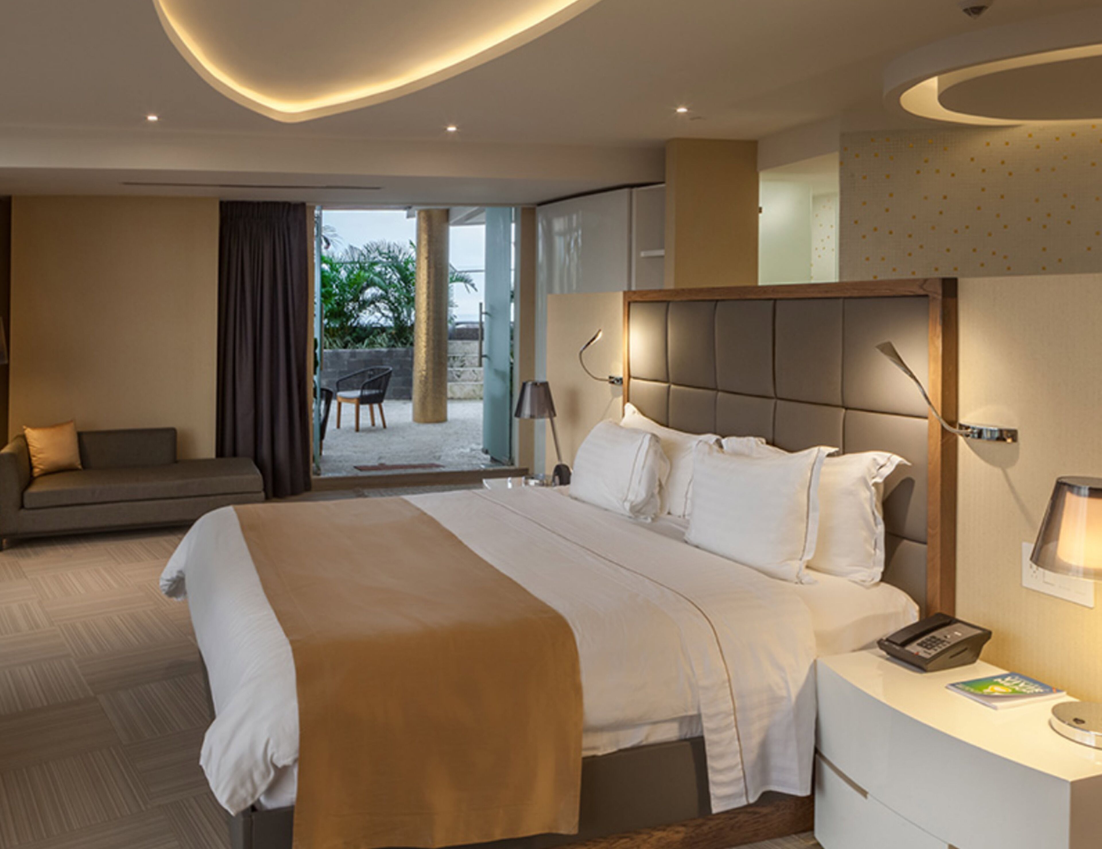 Una habitación de hotel moderna con una cama grande, un sofá, un escritorio con lámpara y vistas al exterior.