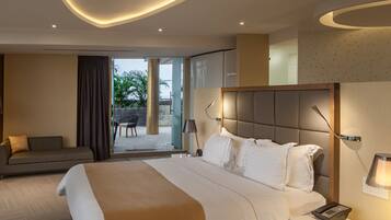A modern hotel room with a large bed, a sofa, a desk with a lamp, and a view of the outdoors.