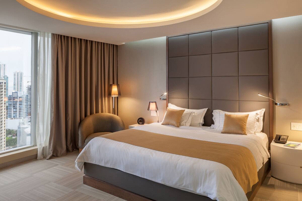 Een moderne hotelkamer met een groot bed, uitzicht over de stad en een sfeervolle verlichting.