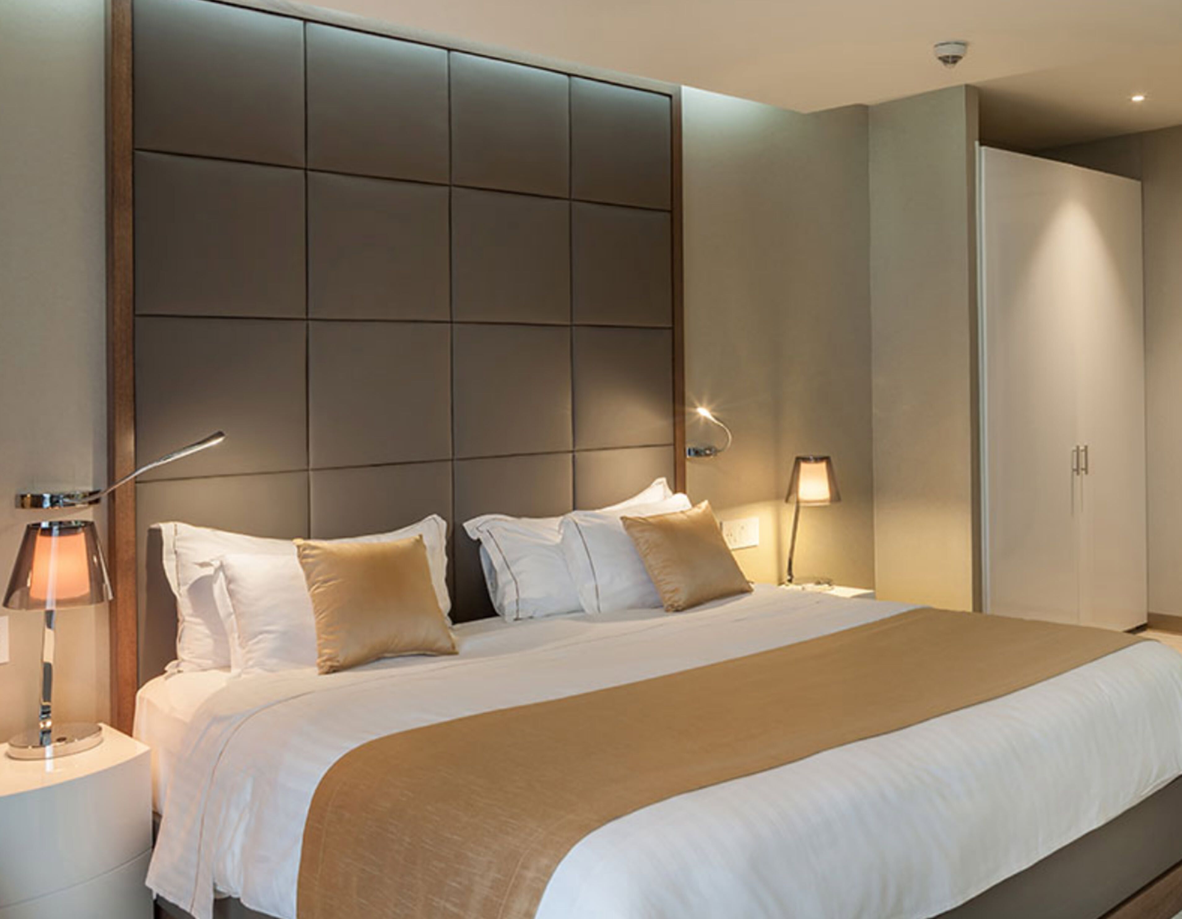 Una habitación de hotel moderna con una cama grande, cabecera de diseño tipo entramado, lámparas de noche y un armario.