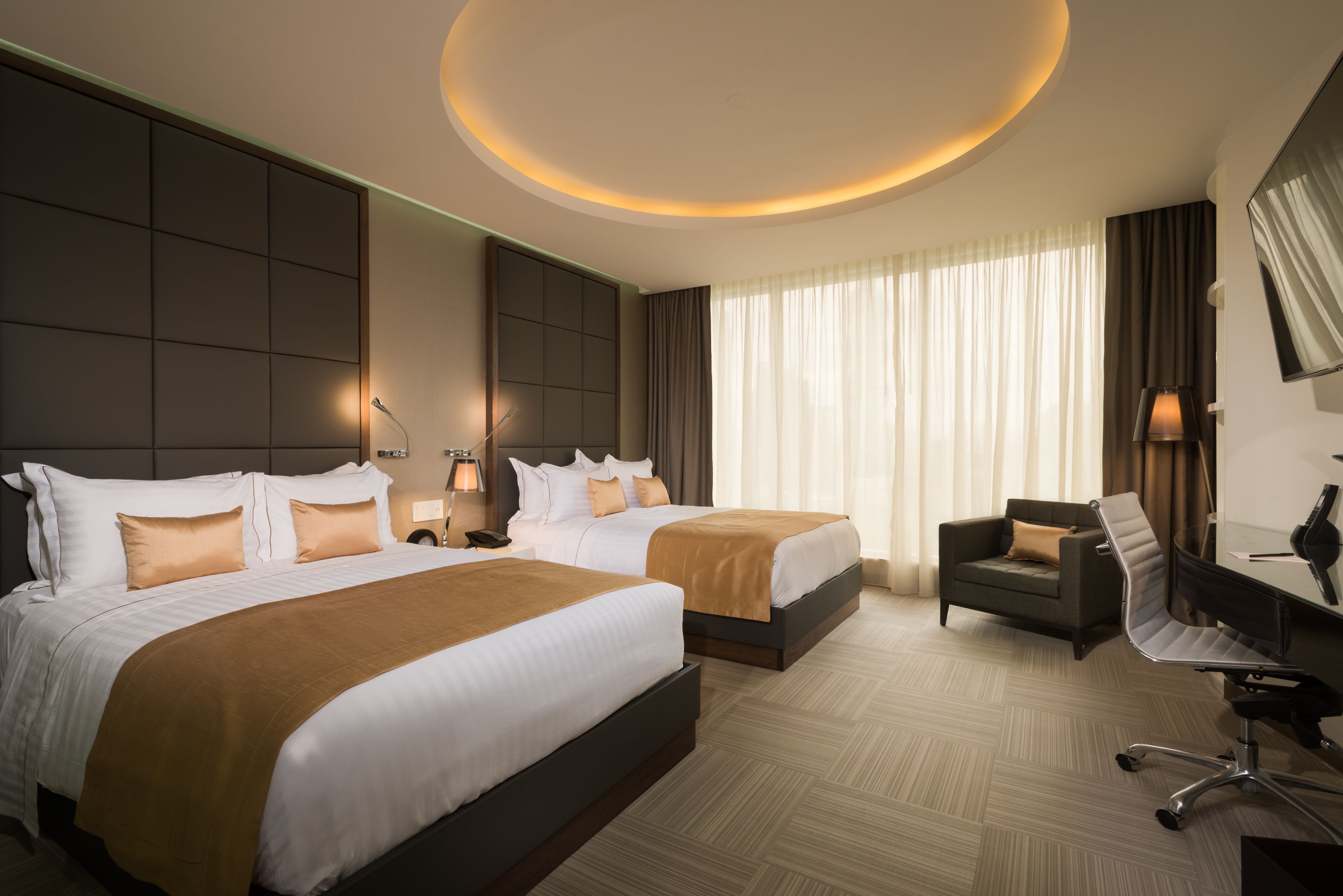 A hotel room with two beds, a desk, a chair, and a large window with curtains.