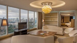 Una habitación de hotel moderna con un ventanal amplio que ofrece vistas a la ciudad, un candelabro y una zona de estar acogedora.