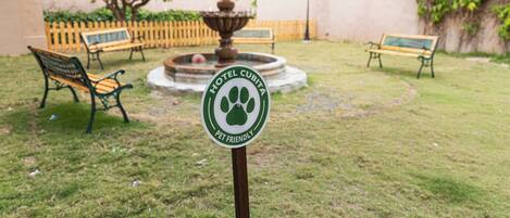 Placa de hotel indicando que aceita animais de estimação, rodeada por uma fonte, bancos e um gramado bem cuidado.