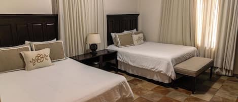 Habitación de hotel con dos camas, una mesita de noche, una lámpara y un ventanal con cortinas.