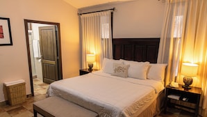 A neatly arranged bedroom with a large bed, bedside tables with lamps, a bench, and a mirror on the wall. - Hotel Cubitá Boutique Resort & Spa (La Arena)